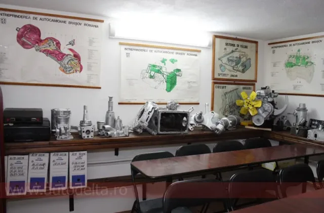Planșe cu schema motorului și piese auto expuse pe rafturi în sala de curs